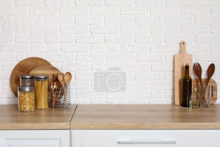 Téléchargez les photos : Comptoir en bois avec planches à découper et ustensiles près du mur de briques blanches - en image libre de droit