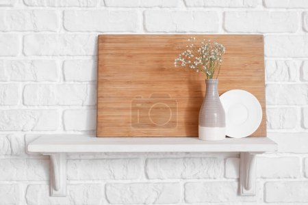 Téléchargez les photos : Étagère de cuisine avec planche à découper, assiette et vase à fleurs suspendus au mur de briques blanches - en image libre de droit