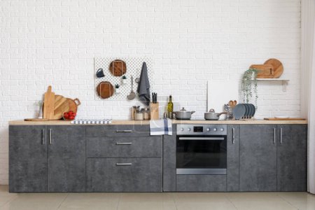 Téléchargez les photos : Comptoirs gris avec planches à découper, ustensiles, four et cuisinière électrique dans la cuisine moderne - en image libre de droit