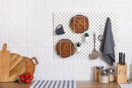 Téléchargez les photos : Pegboard avec planches à découper, plante d'intérieur et ustensiles suspendus au mur de briques blanches dans la cuisine - en image libre de droit