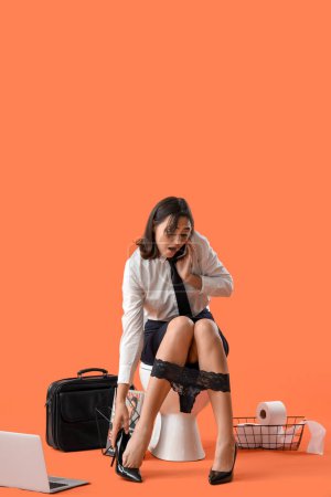 Téléchargez les photos : Stressé jeune femme d'affaires parlant par téléphone portable sur cuvette de toilette sur fond orange - en image libre de droit
