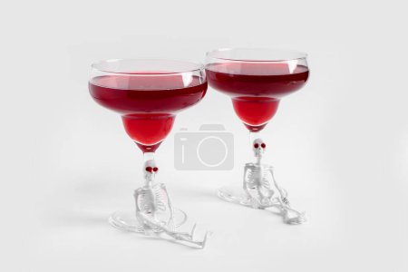 Téléchargez les photos : Lunettes de délicieux cocktail avec squelettes pour la célébration d'Halloween sur fond blanc - en image libre de droit
