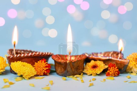 Photo for Diya lamps with beautiful flowers on blue table against blurred lights. Divaly celebration - Royalty Free Image