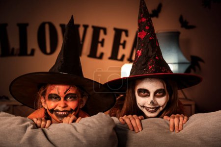 Photo for Little girls dressed for Halloween behind sofa at home in evening - Royalty Free Image