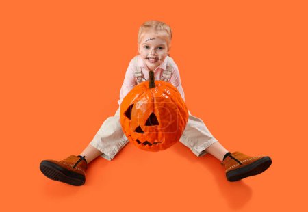 Téléchargez les photos : Petite fille mignonne habillée pour Halloween comme épouvantail avec citrouille sur fond orange - en image libre de droit