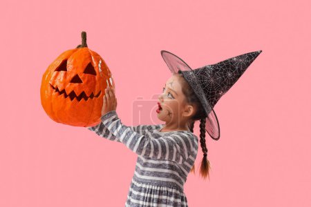 Téléchargez les photos : Petite fille mignonne habillée pour Halloween en sorcière avec citrouille sur fond rose - en image libre de droit