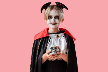Téléchargez les photos : Petit garçon habillé pour Halloween comme vampire avec crâne sur fond rose - en image libre de droit