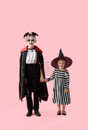 Téléchargez les photos : Petits enfants habillés pour Halloween tenant la main sur fond rose - en image libre de droit
