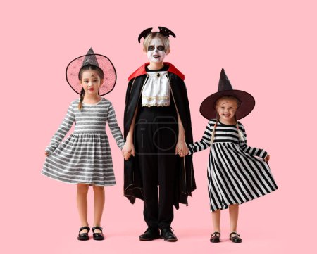 Téléchargez les photos : Petits enfants habillés pour Halloween tenant la main sur fond rose - en image libre de droit