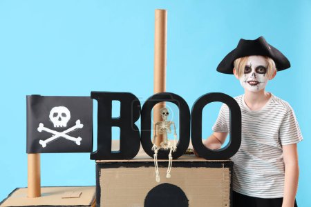 Téléchargez les photos : Petit garçon habillé pour Halloween en pirate avec navire en carton sur fond bleu - en image libre de droit