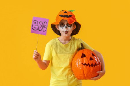 Téléchargez les photos : Petit garçon habillé pour Halloween avec le mot BOO et citrouille sur fond jaune - en image libre de droit