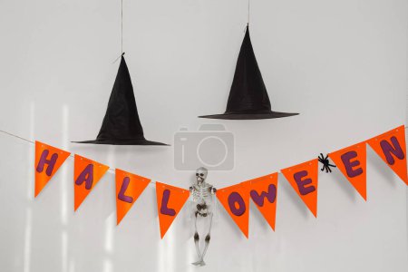 Photo for Flags with word HALLOWEEN, skeleton and witch hats near light wall - Royalty Free Image
