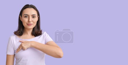 Téléchargez les photos : Jeune femme vérifiant son sein sur fond lilas avec de l'espace pour le texte - en image libre de droit