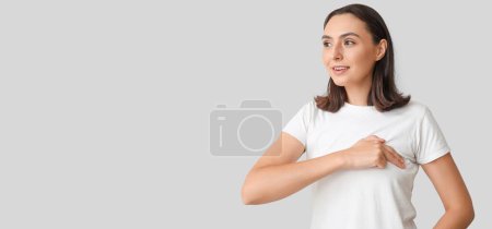 Téléchargez les photos : Jeune femme vérifiant sa poitrine sur fond gris avec espace pour le texte - en image libre de droit