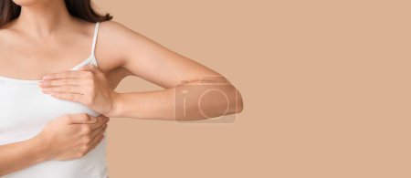Téléchargez les photos : Jeune femme vérifiant sa poitrine sur fond beige avec espace pour le texte - en image libre de droit