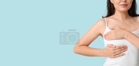 Téléchargez les photos : Jeune femme vérifiant sa poitrine sur fond bleu clair avec de l'espace pour le texte - en image libre de droit