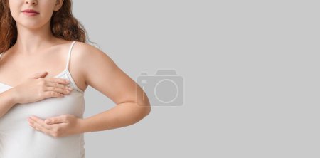 Téléchargez les photos : Jeune femme vérifiant sa poitrine sur fond gris avec espace pour le texte - en image libre de droit
