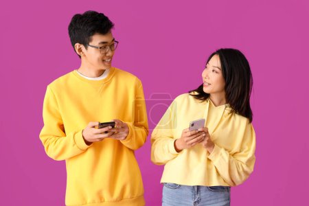 Foto de Jóvenes amigos asiáticos usando teléfonos móviles sobre fondo violeta - Imagen libre de derechos