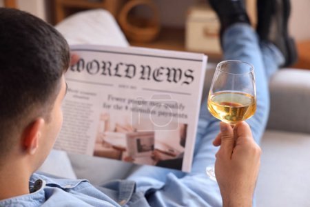 Photo for Young man with glass of wine reading newspaper at home, closeup - Royalty Free Image