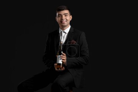 Photo for Young sommelier with bottle of wine sitting on black background - Royalty Free Image