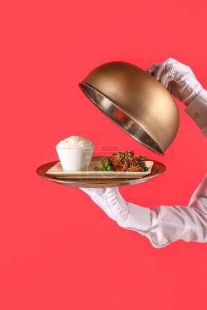 Téléchargez les photos : Serveur avec plateau de savoureux poulet chinois et riz sur fond rouge - en image libre de droit