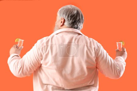 Téléchargez les photos : Portrait d'homme âgé avec des photos de tequila sur fond orange, vue de dos - en image libre de droit