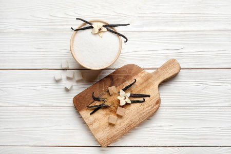 Board with aromatic vanilla sugar, flowers and sticks on white wooden background