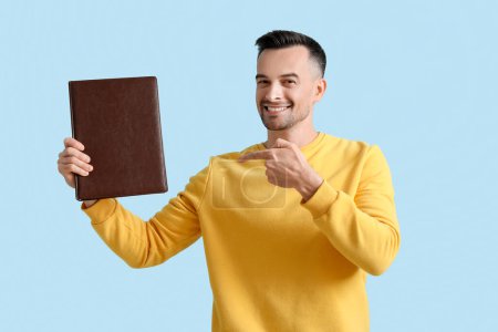 Photo for Happy young man pointing at photo album on blue background - Royalty Free Image