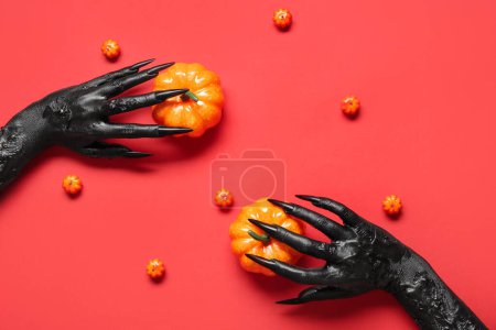 Téléchargez les photos : Mains noires de sorcière avec des citrouilles sur fond rouge. Fête d'Halloween - en image libre de droit