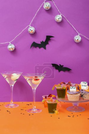 Téléchargez les photos : Composition de fête d'Halloween avec cupcakes, martini et décorations sur table orange sur fond violet - en image libre de droit
