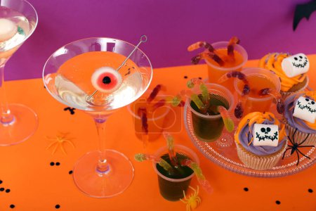 Téléchargez les photos : Composition de fête d'Halloween avec cupcakes, martini et décorations sur table orange sur fond violet - en image libre de droit