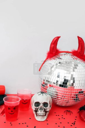 Téléchargez les photos : Composition de fête d'Halloween avec poinçon, crâne et boule disco sur table rouge sur fond blanc - en image libre de droit