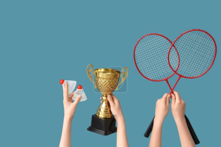 Photo for Female hands with gold cup, badminton rackets and shuttlecocks on blue background - Royalty Free Image