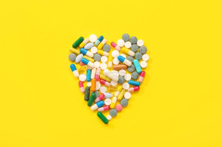 Foto de Corazón hecho de diferentes píldoras sobre fondo amarillo - Imagen libre de derechos