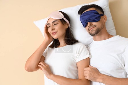 Téléchargez les photos : Jeune couple en masques de couchage avec oreiller sur fond beige - en image libre de droit