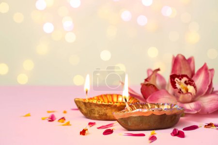 Photo for Diya lamps with orchid flowers on pink table against blurred lights. Divaly celebration - Royalty Free Image