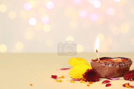 Photo for Diya lamp with beautiful flowers on beige table against blurred lights. Divaly celebration - Royalty Free Image
