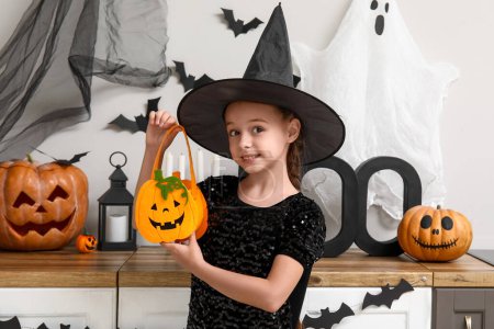 Téléchargez les photos : Petite fille mignonne habillée en sorcière avec sac et citrouilles dans la cuisine décorée pour Halloween - en image libre de droit