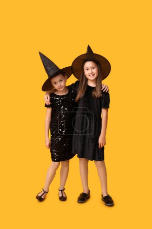 Téléchargez les photos : Petites filles mignonnes habillées pour Halloween comme des sorcières sur fond jaune - en image libre de droit