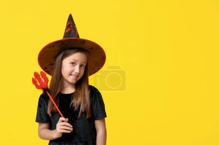 Téléchargez les photos : Petite fille mignonne habillée pour Halloween comme une sorcière avec fourche diable rouge sur fond jaune - en image libre de droit