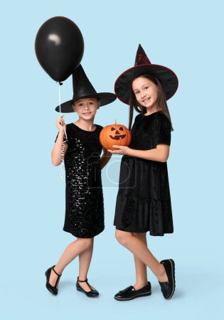Téléchargez les photos : Petites filles mignonnes habillées pour Halloween comme des sorcières avec citrouille et ballon sur fond bleu - en image libre de droit