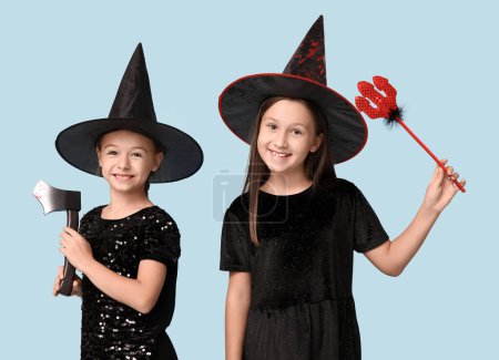 Téléchargez les photos : Petites filles mignonnes habillées pour Halloween comme des sorcières avec hache et fourche diable rouge sur fond bleu - en image libre de droit