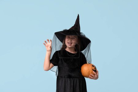 Téléchargez les photos : Petite fille mignonne habillée pour Halloween en sorcière avec citrouille sur fond bleu - en image libre de droit