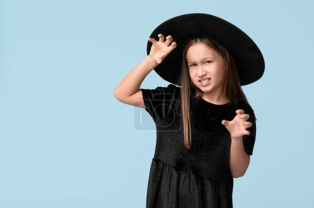 Téléchargez les photos : Petite fille mignonne habillée pour Halloween comme sorcière sur fond bleu - en image libre de droit