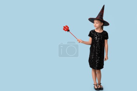 Téléchargez les photos : Petite fille mignonne habillée pour Halloween comme une sorcière avec fourche diable rouge sur fond bleu - en image libre de droit
