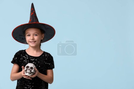 Téléchargez les photos : Petite fille mignonne habillée pour Halloween en sorcière avec crâne humain sur fond bleu - en image libre de droit