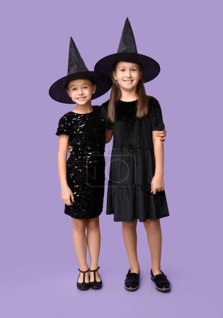 Téléchargez les photos : Petites filles mignonnes habillées pour Halloween comme des sorcières sur fond violet - en image libre de droit