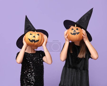 Téléchargez les photos : Petites filles mignonnes habillées pour Halloween comme des sorcières avec des citrouilles sur fond violet - en image libre de droit