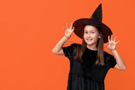 Téléchargez les photos : Petite fille mignonne habillée pour Halloween comme sorcière sur fond orange - en image libre de droit