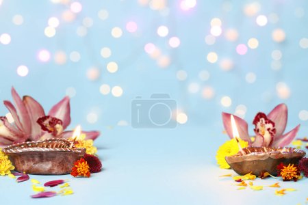 Photo for Diya lamps with beautiful flowers on blue table against blurred lights. Divaly celebration - Royalty Free Image